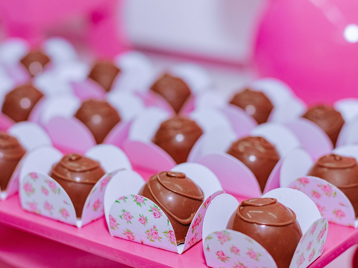 Brigadeiros organizados em forminhas decoradas sobre uma mesa rosa